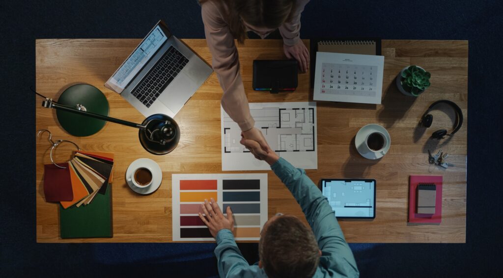 Top view of architects shaking hands at desk with paperwork in office, job interview concept.